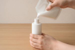 乳白色の詰め替え用パウチから白いポンプボトルに乳液を注いでいる手元の様子